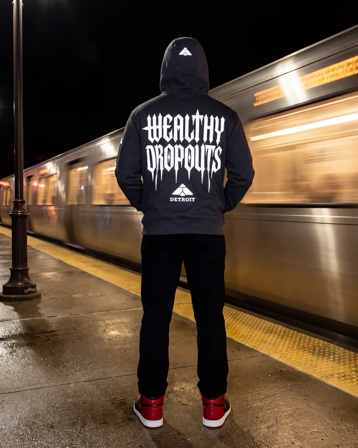Charcoal heather, worn from behind on a platform, hood up, as a train streaks past