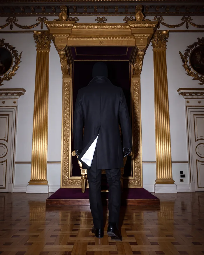 The Pea Coat from behind, collar up, walking to the empty throne, the back vent open on its reflective lining